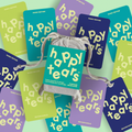 Happy Tears Family Edition deck, Ottawa. Grey linen pouch, rainbow-coloured cards. 'Happy Tears' logo, bilingual text: 'Family connection for all ages', 'Liens familiales pour tous les ages'. Local Ottawa board games.