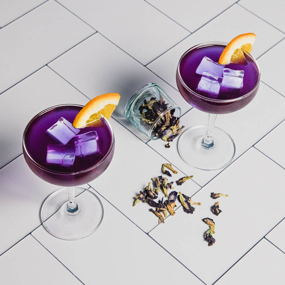 Two purple cocktails with orange slices on a tiled surface