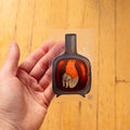 Hand holding a transparent card with a bottle illustration on a wooden surface