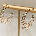Gold hoop earrings on a gold stand against a neutral background