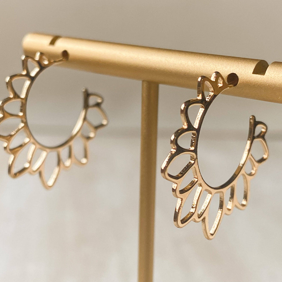 Gold hoop earrings on a gold stand against a neutral background