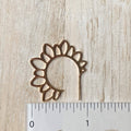 Decorative metal sunflower-shaped object next to a ruler on a wooden surface