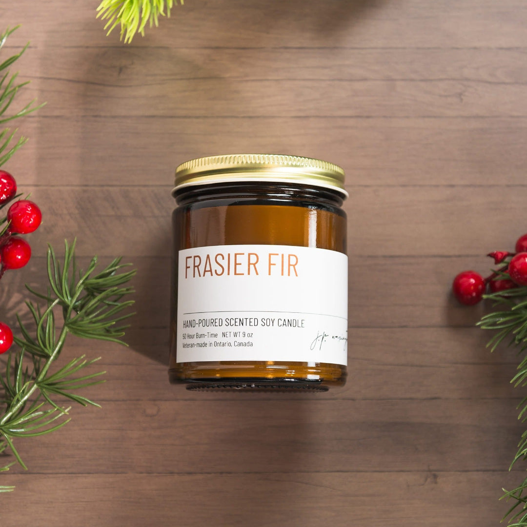 Frasier Fir candle jar on a wooden surface with greenery and berries