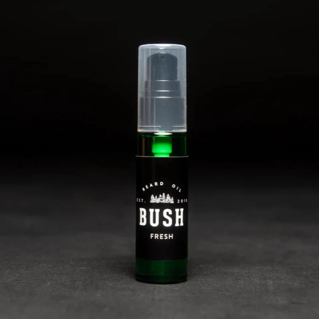 A dark green glass bottle with a black pump dispenser. The bottle is labeled "BUSH" and "FRESH BEARD OIL." The background is black.