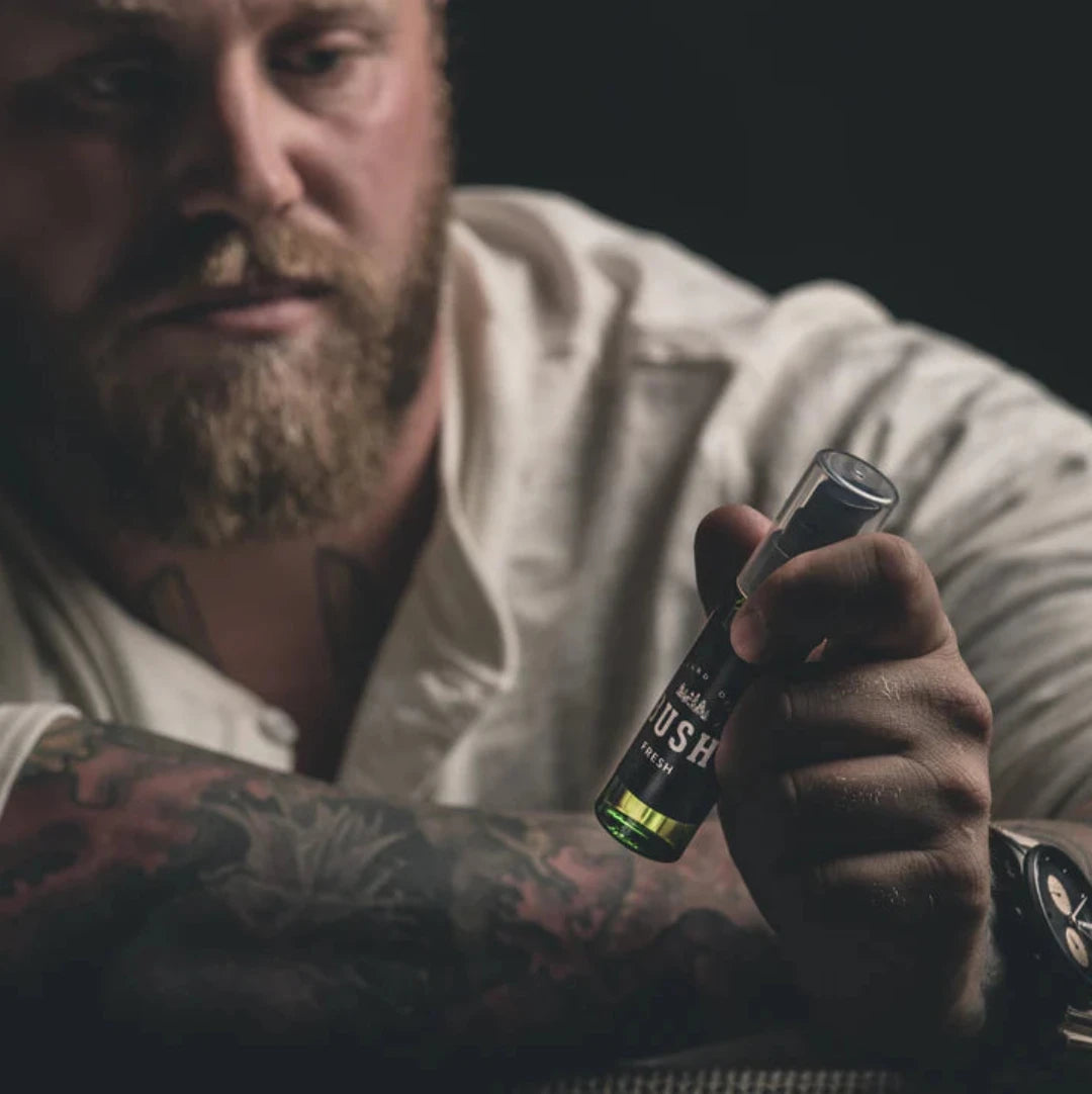 A dark green glass bottle with a black pump dispenser. The bottle is labeled "BUSH" and "FRESH BEARD OIL." The background is black.A dark green glass bottle with a black pump dispenser. The bottle is labeled "BUSH" and "FRESH BEARD OIL." The background is black.