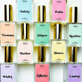 A collection of ten perfume bottles arranged in a grid. Each bottle has a gold cap and a transparent body, revealing the colored liquid inside. Each bottle has a label with the perfume's name and a list of its fragrance notes. The names include Aubrey, Zaida, Gemma, Draper, Harlow, Bianca, Renfrew, Ophelia, Laurent, and Violet.