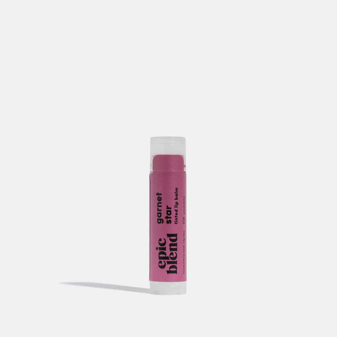 A white tube of Epic Blend Garnet Star Tinted Lip Balm with a deep pink label. The label displays the brand name, "garnet star tinted lip balm," and indicates it has a subtle shimmer.