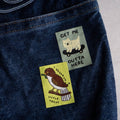 Two stickers on a denim surface, one with a dog and text, the other with a bird and text.