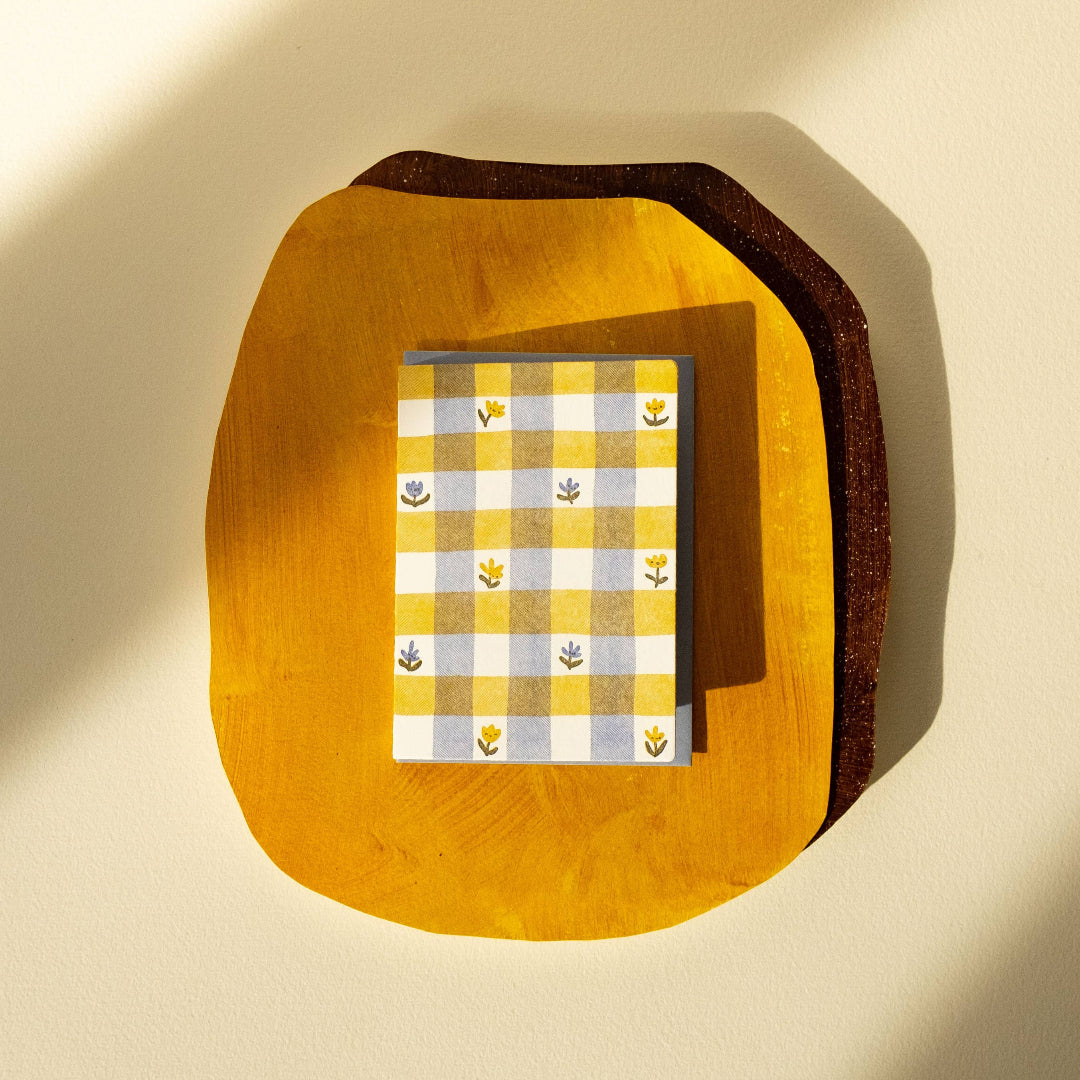 Notebook with yellow and white checkered cover on a wooden stand against a beige background