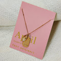 A gold necklace with a quartz stone pendant. The pendant also has the word "STRENGTH" engraved on it. The necklace is displayed on a pink card with the month "April" and the brand name "Foxy Originals."