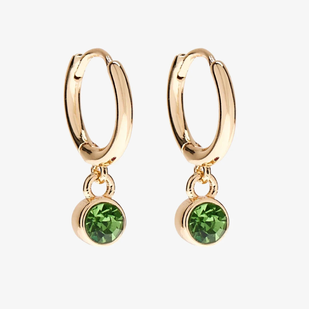 A set of three pairs of peridot earrings displayed on a green card. The set includes a pair of stud earrings, a pair of bar earrings with small peridot beads, and a pair of hoop earrings with dangling peridot stones. The card has the month "August" and the brand name "Foxy Originals."