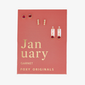 A set of three pairs of garnet earrings displayed on a red card. The set includes a pair of stud earrings, a pair of bar earrings with small garnet beads, and a pair of hoop earrings with dangling garnet stones. The card has the month "January" and the brand name "Foxy Originals."