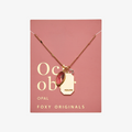 A gold necklace with an opal stone pendant. The pendant also has the word "HEALING" engraved on it. The necklace is displayed on a pink card with the month "October" and the brand name "Foxy Originals."