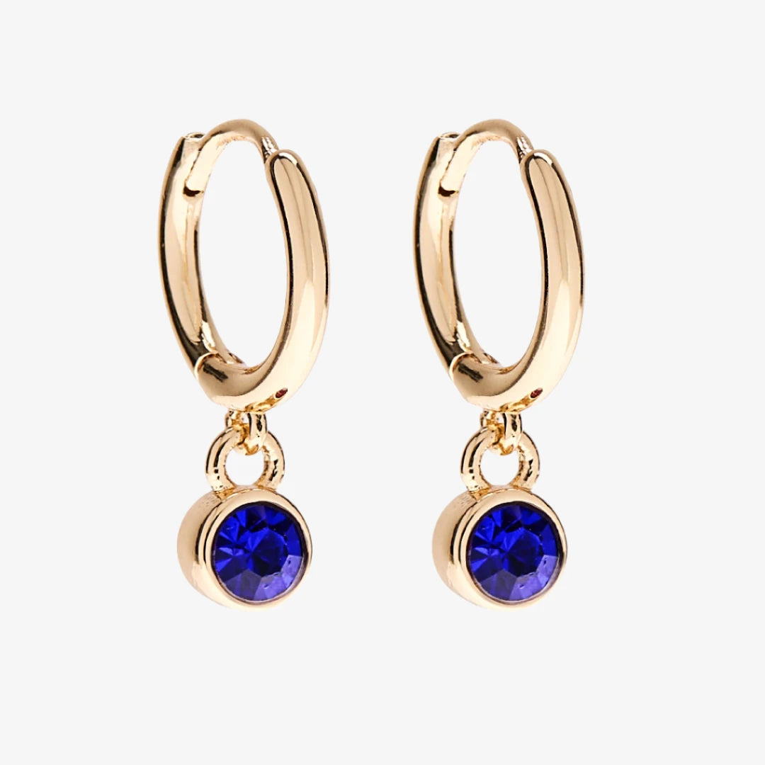 A set of three pairs of sapphire earrings displayed on a blue card. The set includes a pair of stud earrings, a pair of bar earrings with small sapphire beads, and a pair of hoop earrings with dangling sapphire stones. The card has the month "September" and the brand name "Foxy Originals."