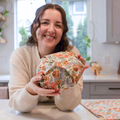 Woman holding a floral-patterned fabric-covered object in a kitchen.