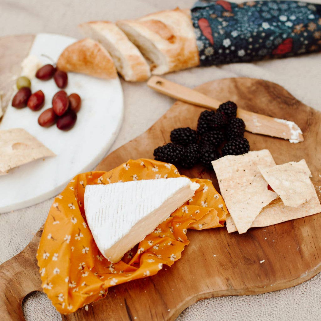 Wooden cutting board with cheese, crackers, and fruit on a neutral background