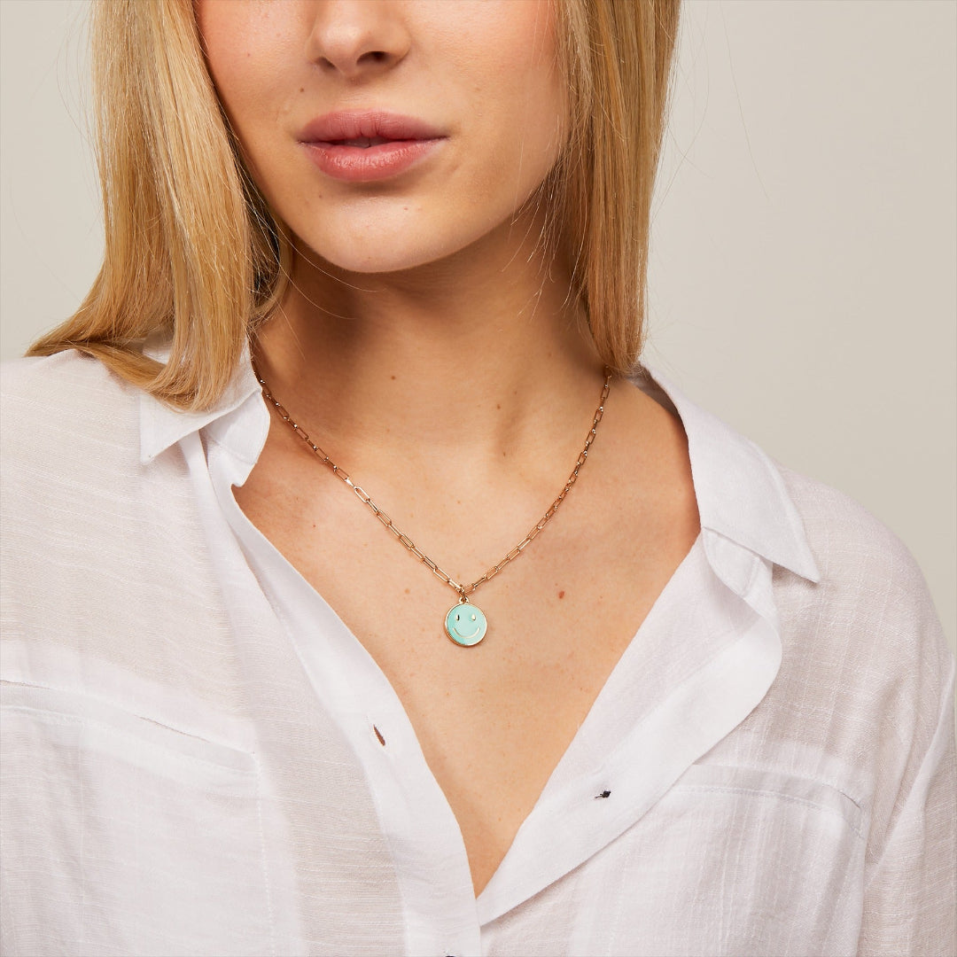 Woman wearing a necklace with a green pendant against a neutral background