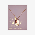 A gold necklace with an amethyst stone pendant. The pendant also has the word "WISDOM" engraved on it. The necklace is displayed on a purple card with the month "February" and the brand name "Foxy Originals."