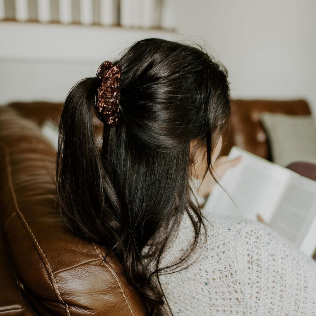 Person sitting on a brown leather couch reading a book with a neutral background