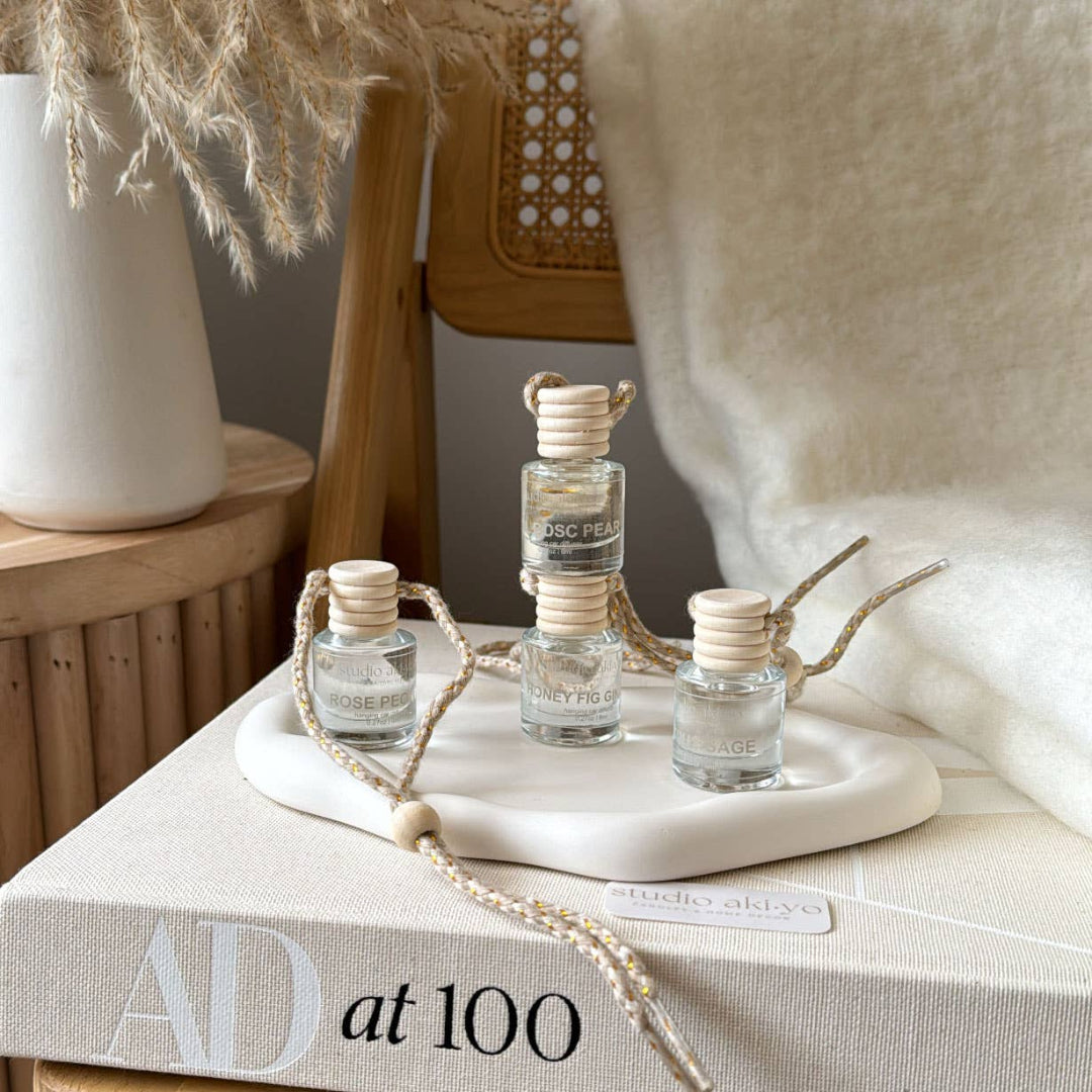Three small glass bottles with wooden caps on a white tray, placed on a textured surface with a magazine in the background.