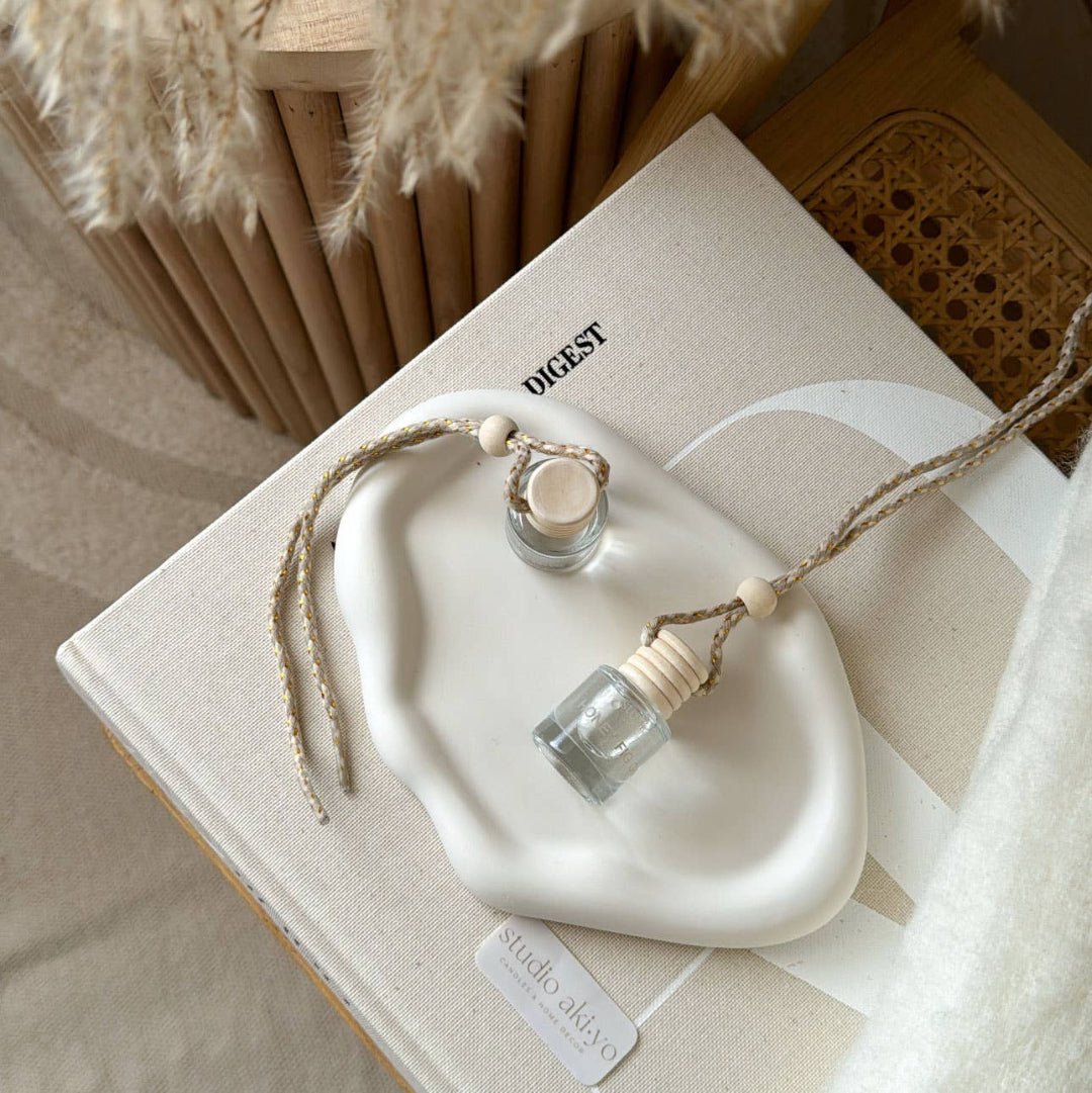 White decorative tray with small bottles on a beige surface, featuring the brand 'studio okiyo'.