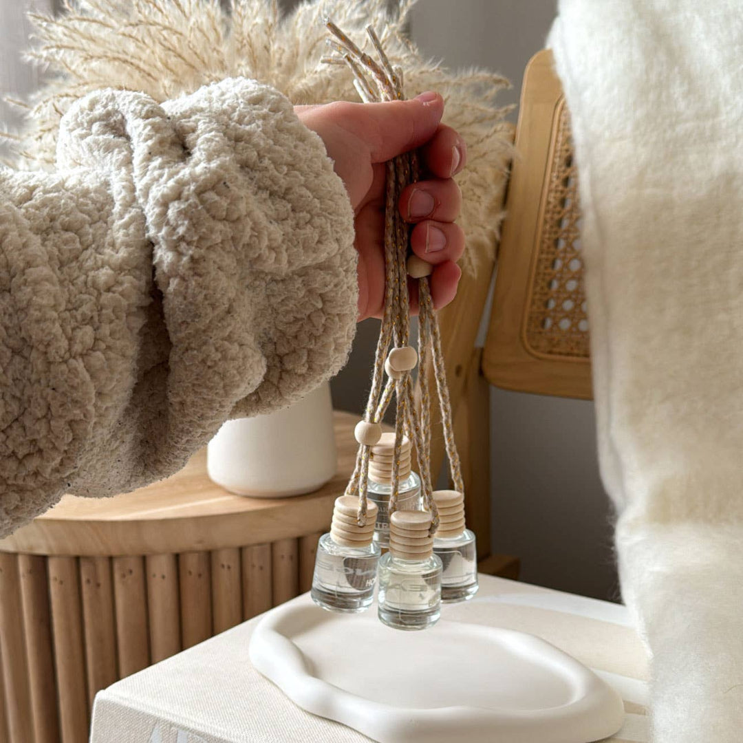 Person holding a decorative item with small bottles and beads, wearing a textured sweater.