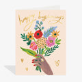 Greeting card with hand holding flowers and 'Happy Beginnings' text on a beige background