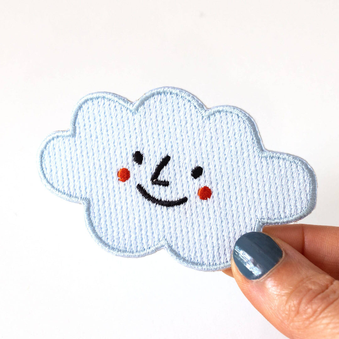 Smiley face cloud patch held by a hand on a white background