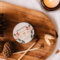 Round product packaging with branding on a wooden tray with candles and pinecones.