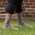 A pair of grey men's crew socks with orange, white, and black abstract lines. One sock features a cartoon drawing of a man with an orange background and the text "HERE COMES COOL DAD" and "HIGH FIVE".