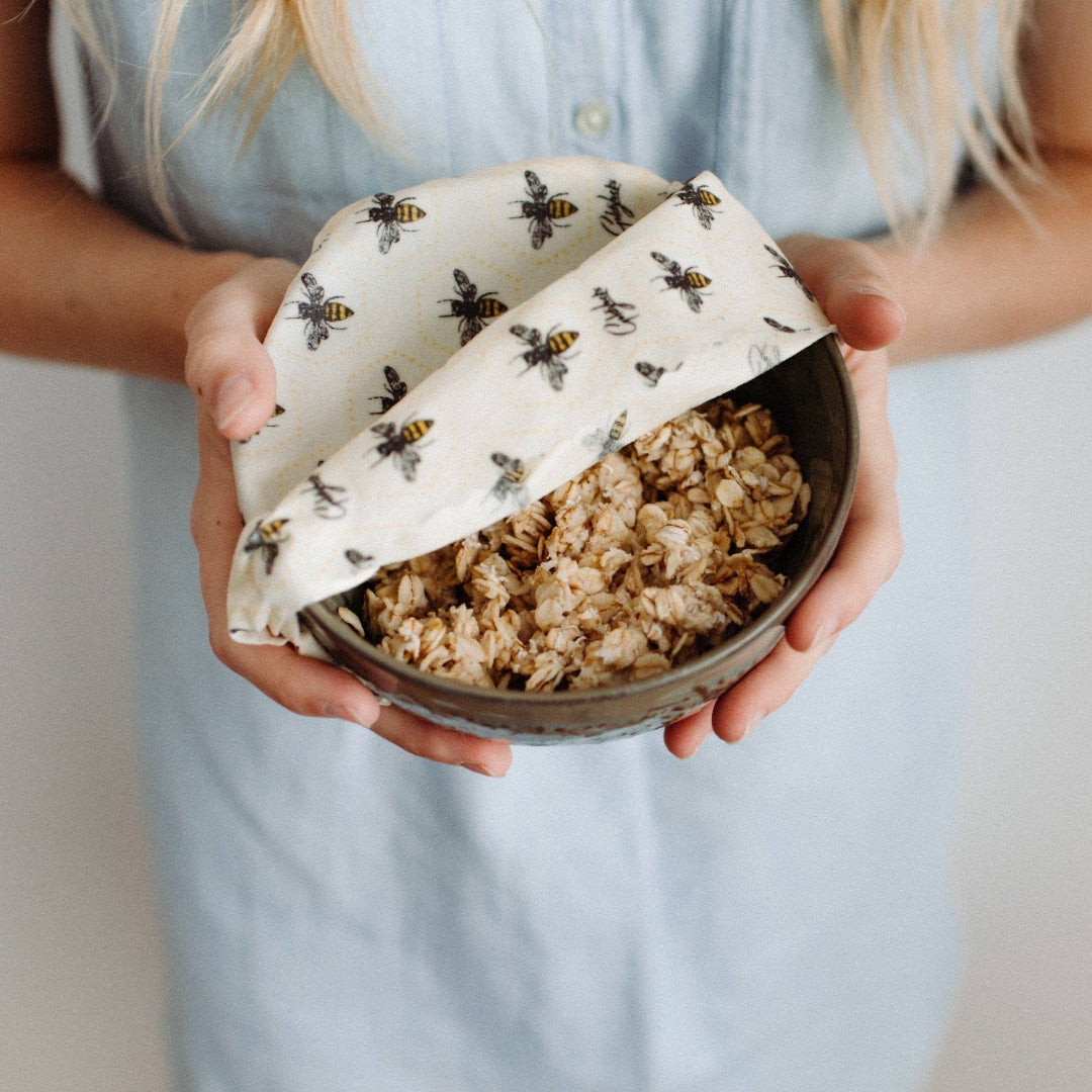 Person holding a bowl of granola wrapped in a beeswax wrap with a neutral background