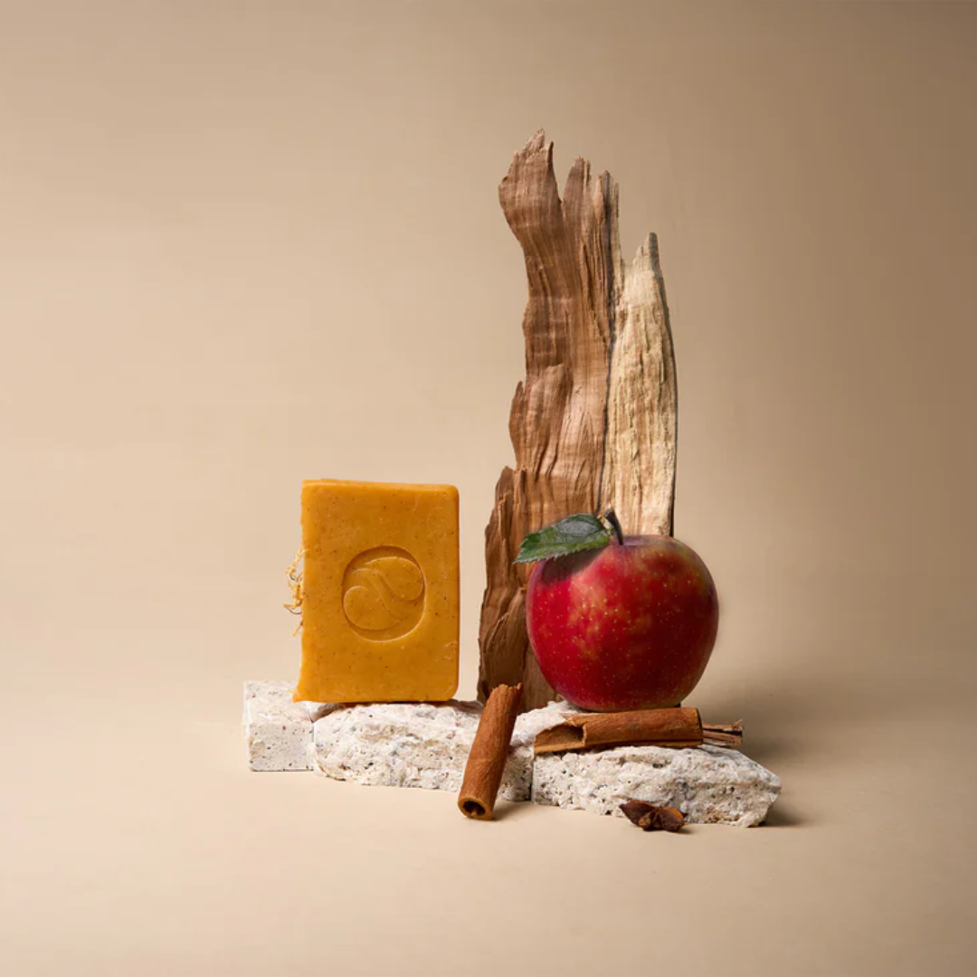 A bar of Aide Bodycare Honeycrisp Cider Soap, featuring a light yellow-orange color and a paper label with the 'aide' logo and 'Honeycrisp Cider' text, displayed on a light-colored surface with a shadow overlay. The soap is natural and handmade, available in Ottawa, Ontario, Canada.