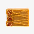 Three bars of yellow soap with visible seeds on a white background