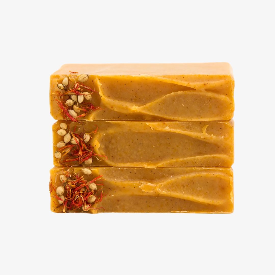 Three bars of yellow soap with visible seeds on a white background