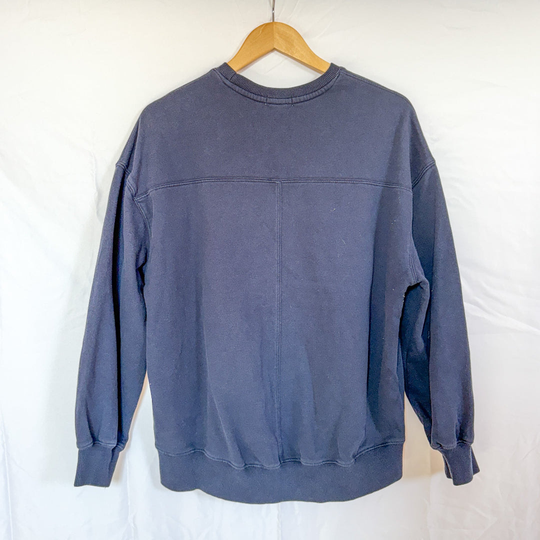 The back view of the same navy blue crewneck sweatshirt, hanging on a wooden hanger against a white background.