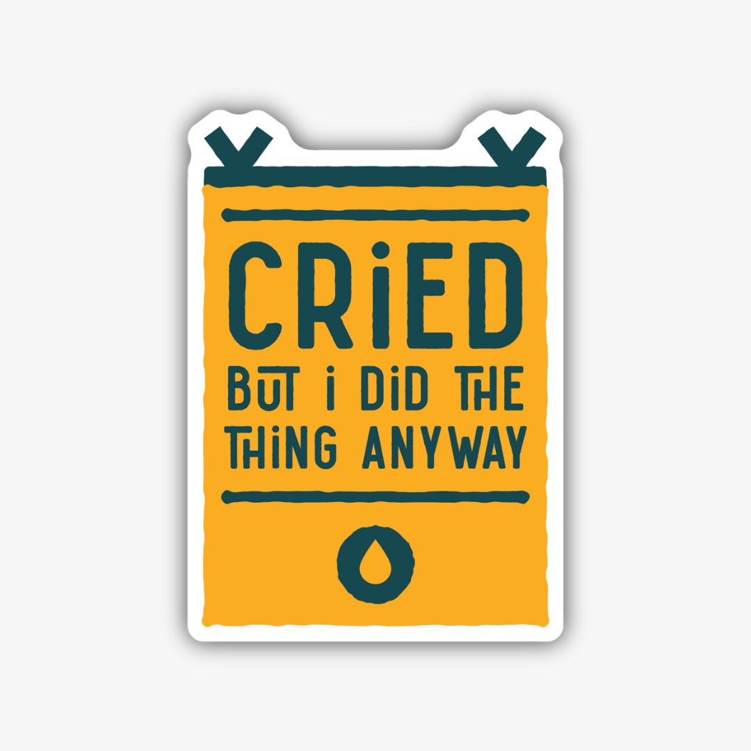 A rectangular banner-shaped sticker with a bold black outline and a golden yellow background. The text "CRIED" is prominently displayed in large dark teal letters, followed by "BUT I DID THE THING ANYWAY" in smaller dark teal text. A single dark teal teardrop icon is at the bottom.