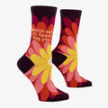 A pair of women's crew socks with a dark purple background and a vibrant, large floral pattern in shades of red, fuchsia, pink, and yellow. Text on one sock reads "Watch out. I'll fuckin' hug you."