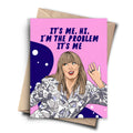 A humorous card featuring a cartoon drawing of Taylor Swift waving. The background is pink with white bubbles, and the text reads, "IT'S ME, HI. I'M THE PROBLEM IT'S ME." A brown kraft envelope is behind the card.