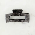 Black marbled hair clip on a white marble surface