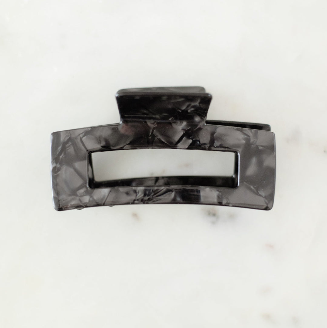 Black marbled hair clip on a white marble surface