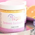 Jar of lemon lavender sugar scrub with a pink and white label on a blurred background.