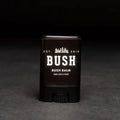 A black lip balm tube with a white label. The label reads "BUSH" and "BUSH BALM FOR LIPS & FACE." The balm is partially twisted up, revealing the product inside. The background is black.