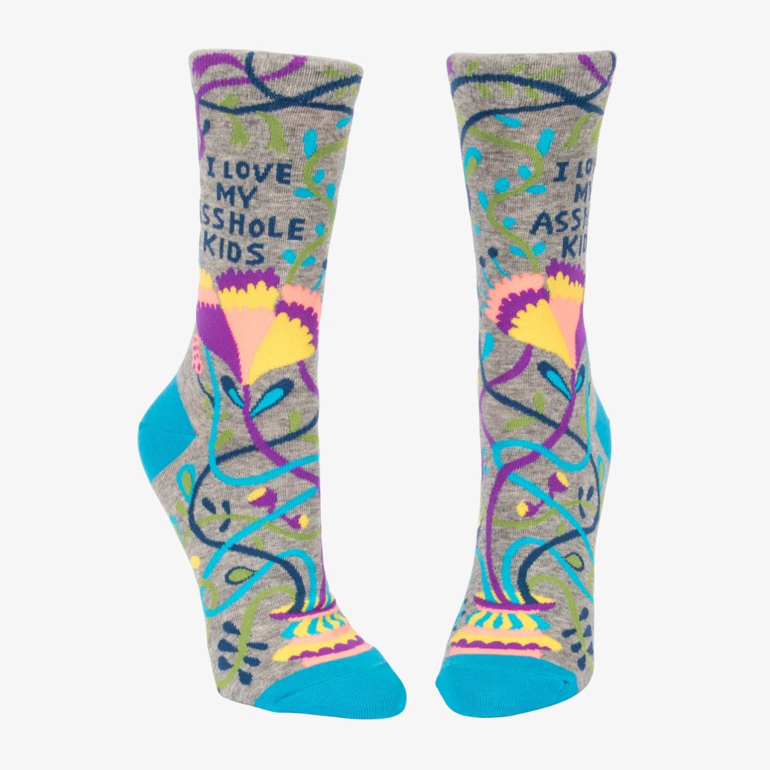 A pair of grey women's crew socks with vibrant, abstract floral and swirling line patterns in purple, yellow, pink, green, and blue. Text on one sock reads "I LOVE MY ASSHOLE KIDS".