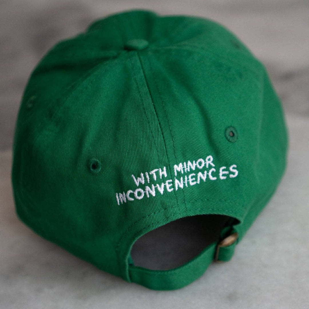 Green cap with text 'WITH MINOR INCONVENIENCES' on a gray surface