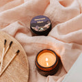 Candle and container on a soft fabric surface with matches nearby