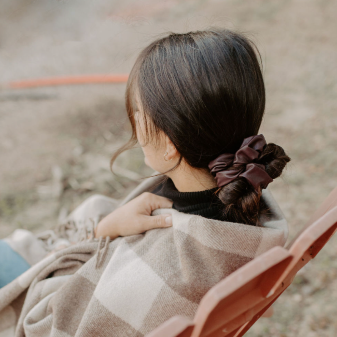 Person sitting outdoors with a plaid blanket and a brown hair scrunchie.
