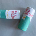 Two 'kiss nature' lip balm containers on a light gray background