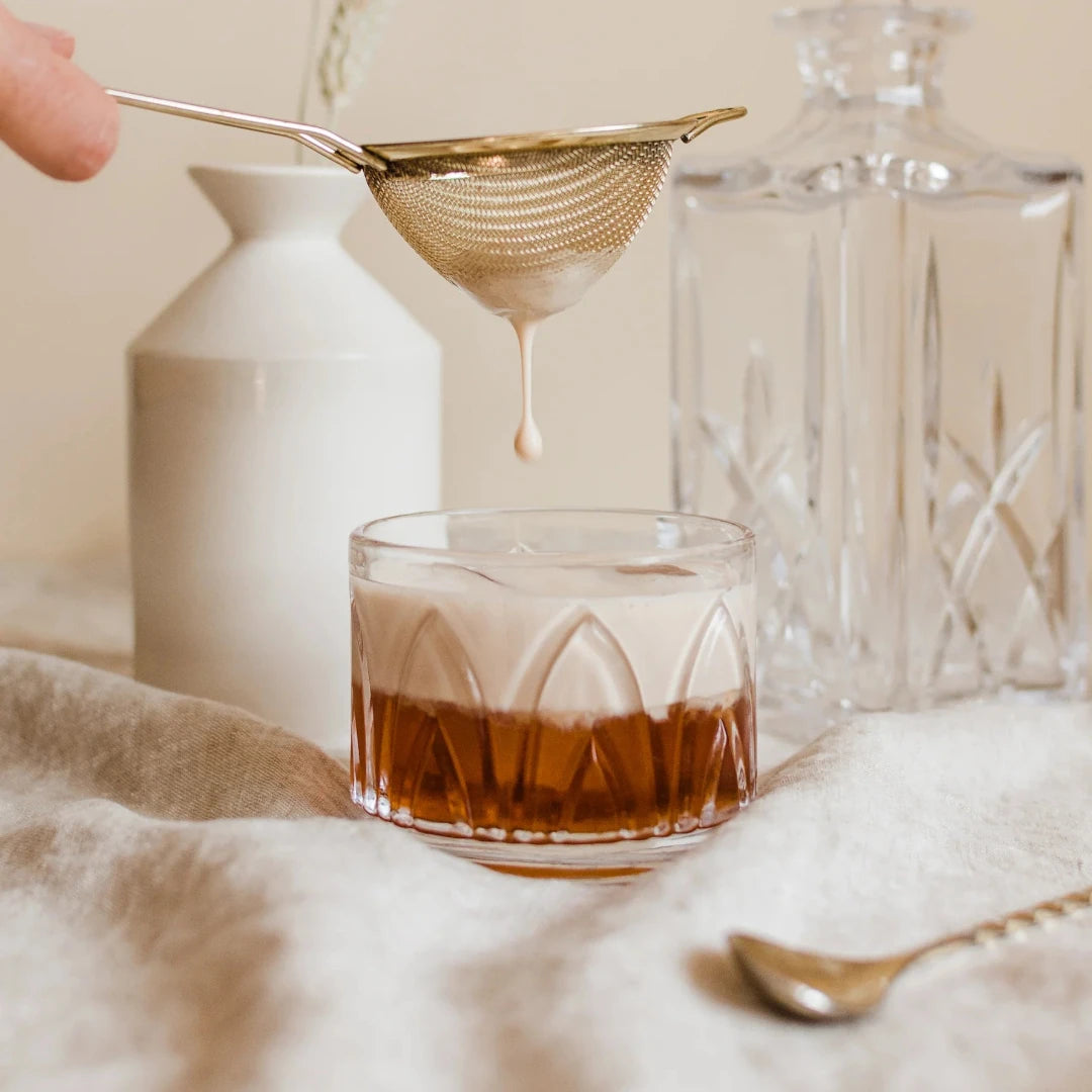 A glass jar filled with dried orange slices, cocoa nibs, and other ingredients. The jar has a white label with the Maiden Voyage logo and the product name "Mocha Old Fashioned Cocktail Infusion."