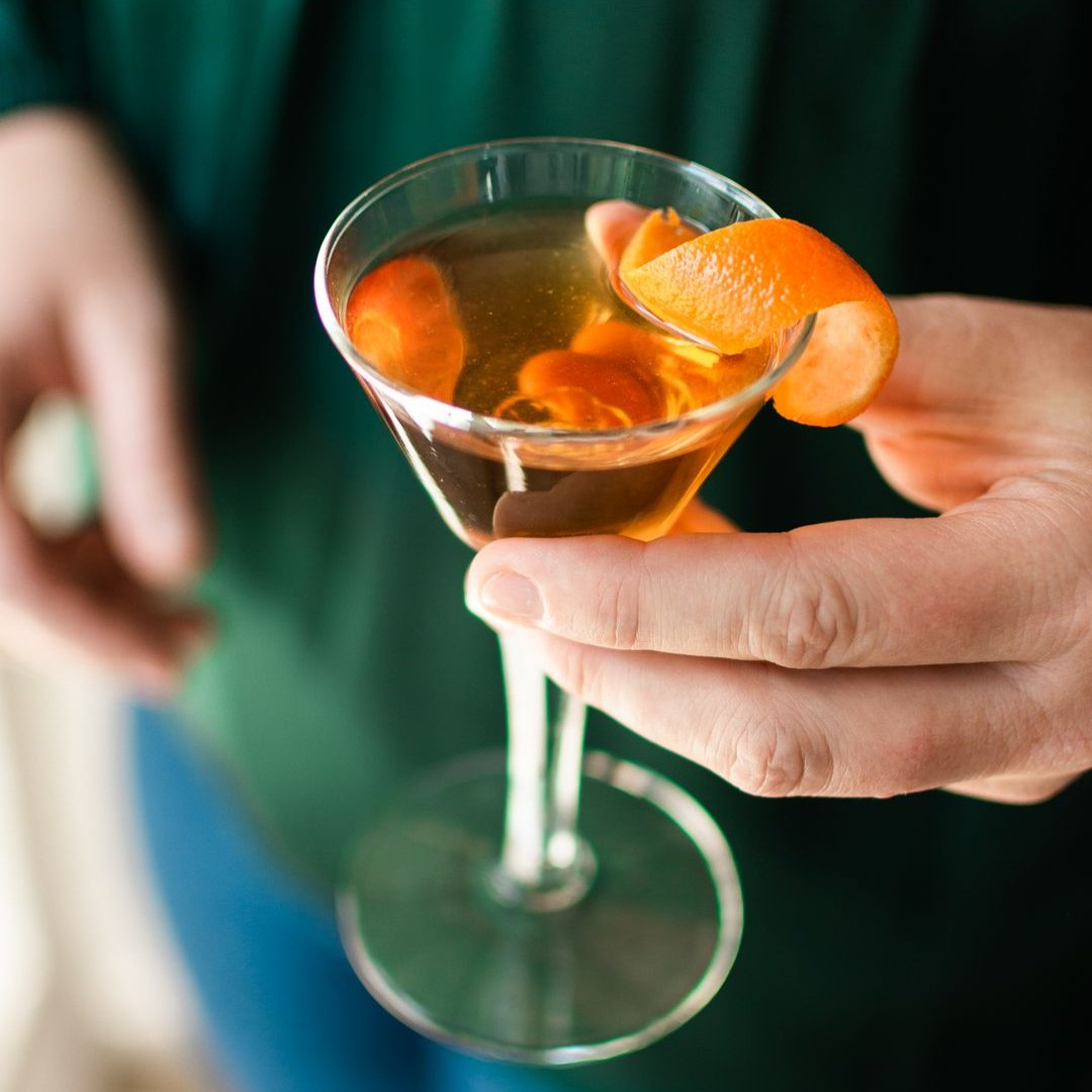 A glass jar filled with dried orange slices, cocoa nibs, and other ingredients. The jar has a white label with the Maiden Voyage logo and the product name "Mocha Old Fashioned Cocktail Infusion."