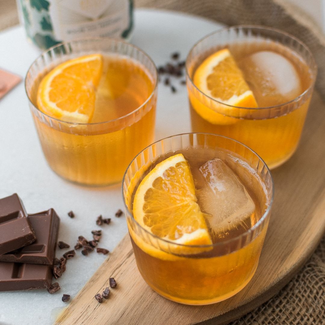 A glass jar filled with dried orange slices, cocoa nibs, and other ingredients. The jar has a white label with the Maiden Voyage logo and the product name "Mocha Old Fashioned Cocktail Infusion."